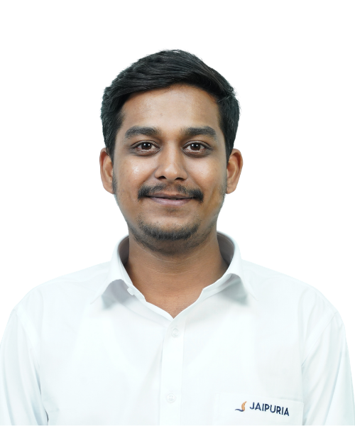 Portrait of a man with short black hair and a light smile, wearing a white button-up shirt with a Jaipuria logo, against a black background.